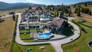 A large, multi-story hotel with a swimming pool, outdoor seating area, and a view of the surrounding mountains.