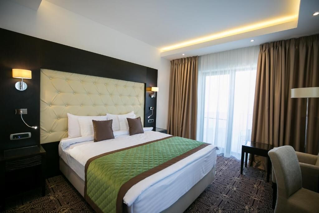 A hotel room with a large bed, a headboard, two bedside tables, a chair, and a window with curtains.