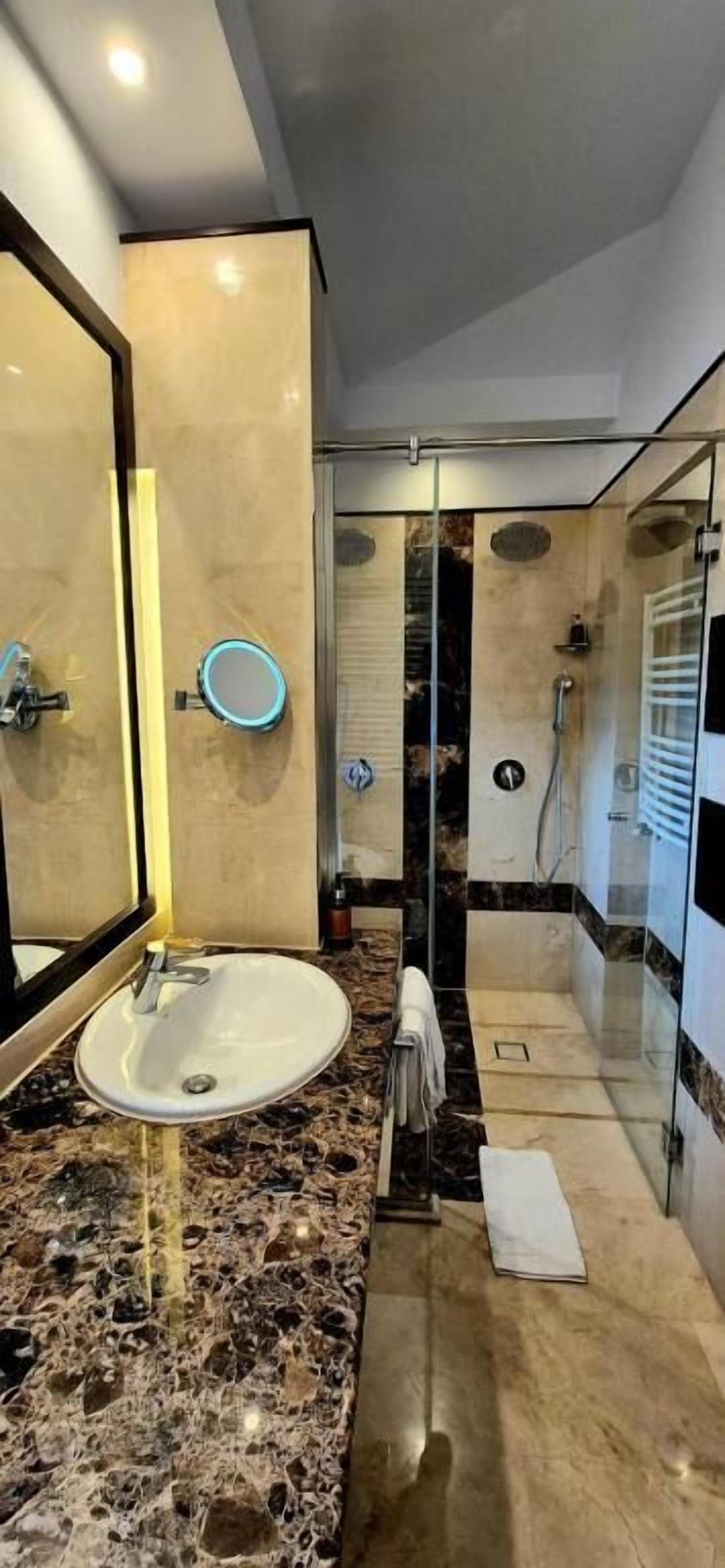 A modern bathroom with a marble sink, a glass shower enclosure, and a large mirror.