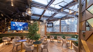 A modern interior with a green sofa, round tables, and chairs, a large TV screen, and a plant.