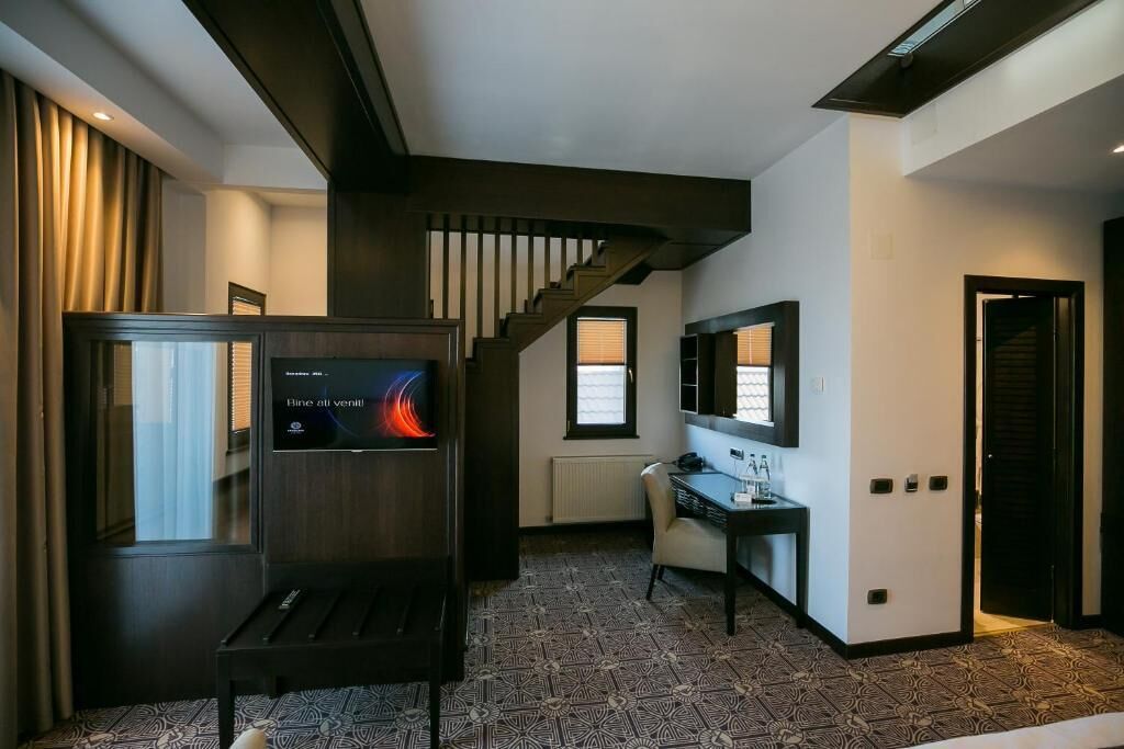 A modern hotel room with a large TV, a desk, and a staircase.