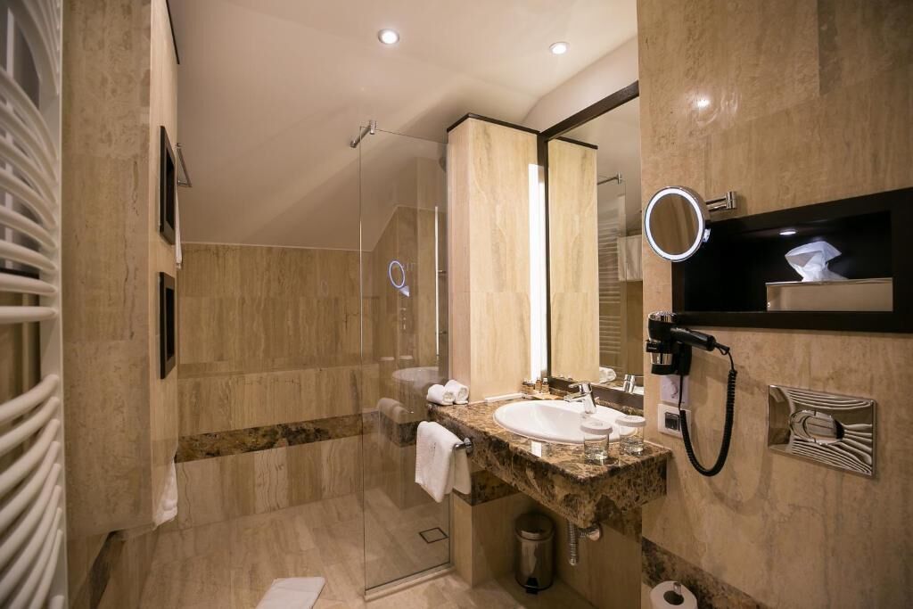 A modern bathroom with a glass shower, a marble sink, and a built-in hairdryer.