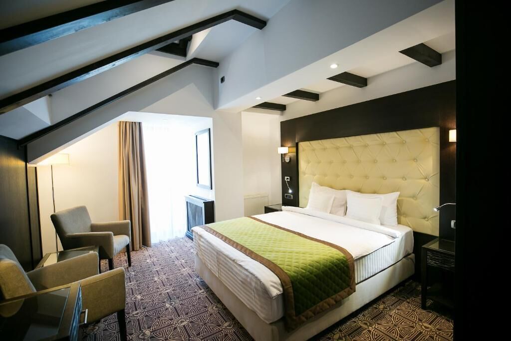 Een moderne hotelkamer met een groot bed, een zithoek met stoelen en uitzicht op het omliggende landschap.