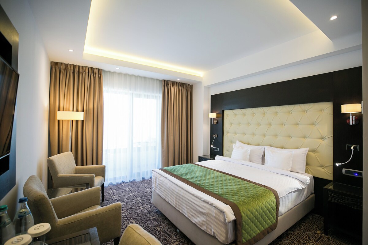 A hotel room with a large bed, two armchairs, a desk with a lamp, and a television.