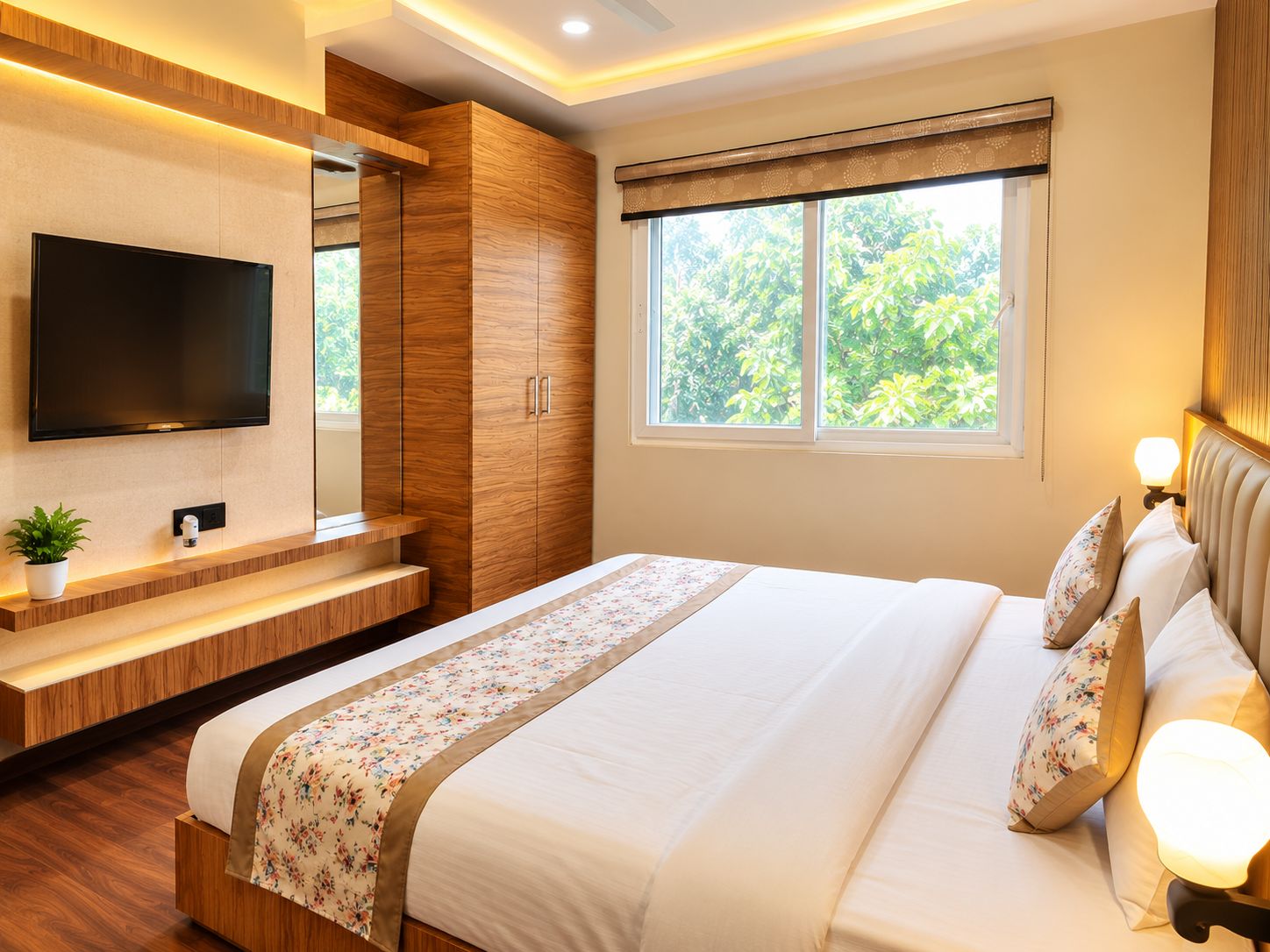 A modern bedroom with a large bed, a TV mounted on the wall, a window with a view of greenery, and built-in wooden furniture.
