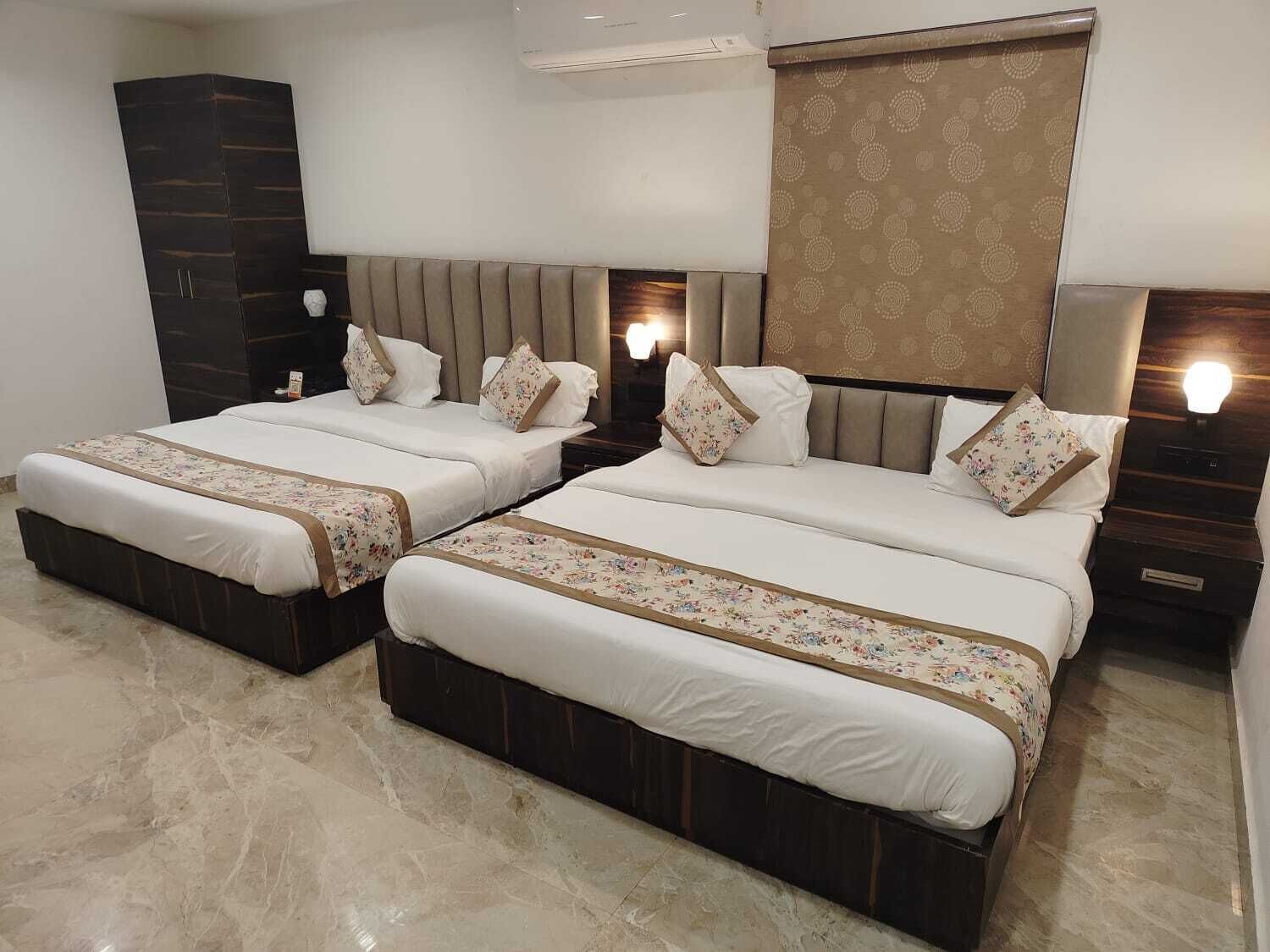 Habitación de hotel con dos camas, un armario de madera oscura, un espejo grande y un cabecero estampado.