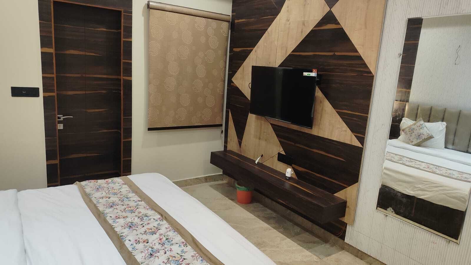 A bedroom with a bed, a TV mounted on the wall, a wooden headboard, and a window with blinds.