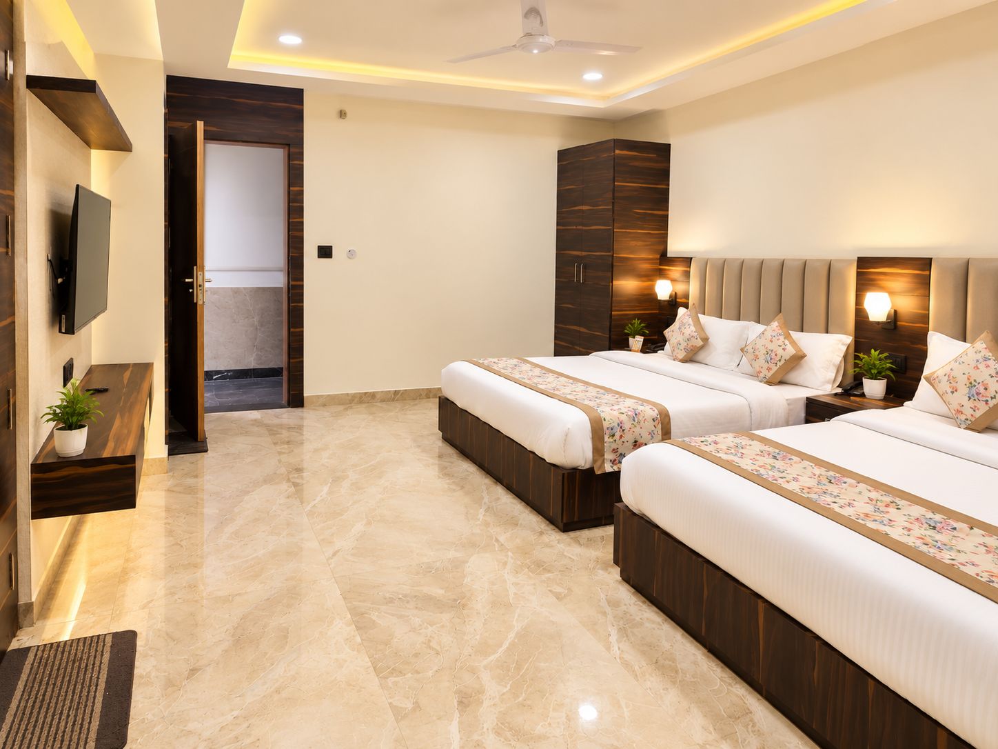 A hotel room with two beds, a TV, a desk with a plant, and a bathroom visible through an open door.