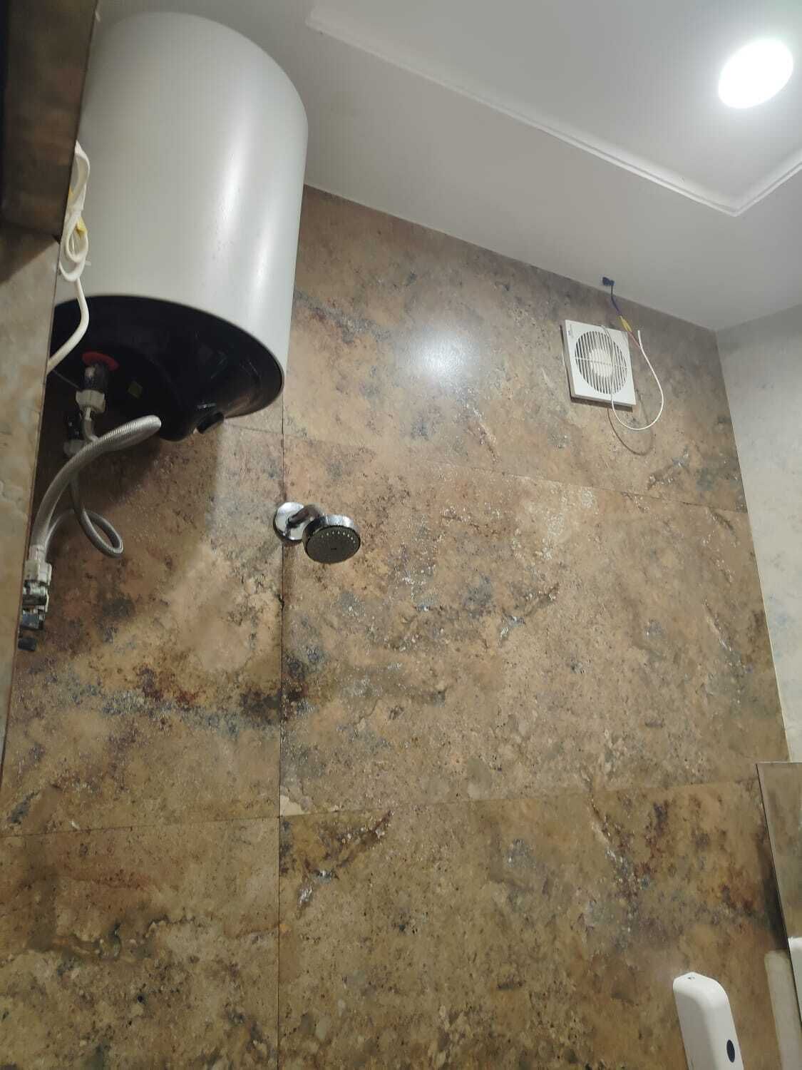 A bathroom with a water heater, a fan, and a marble wall.