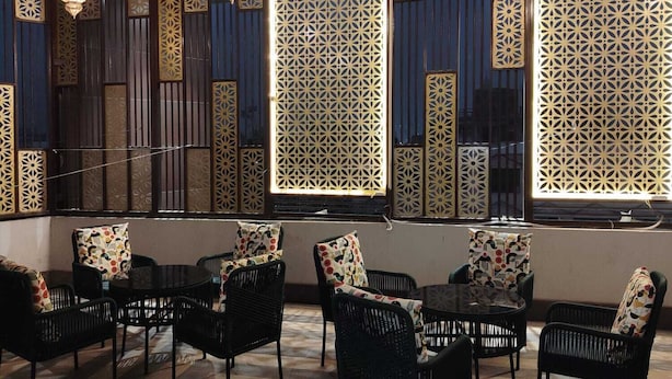 Una habitación con ventanas con diseño, muebles de mimbre negro e iluminación colgante.