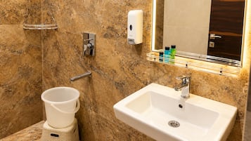 Un bagno con una parete in marmo, un lavandino bianco, un porta asciugamani, un dispenser per sapone e un piccolo cestino.