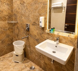 Une salle de bain avec un mur en marbre, un lavabo blanc, un porte-serviettes, un distributeur de savon et une petite poubelle.
