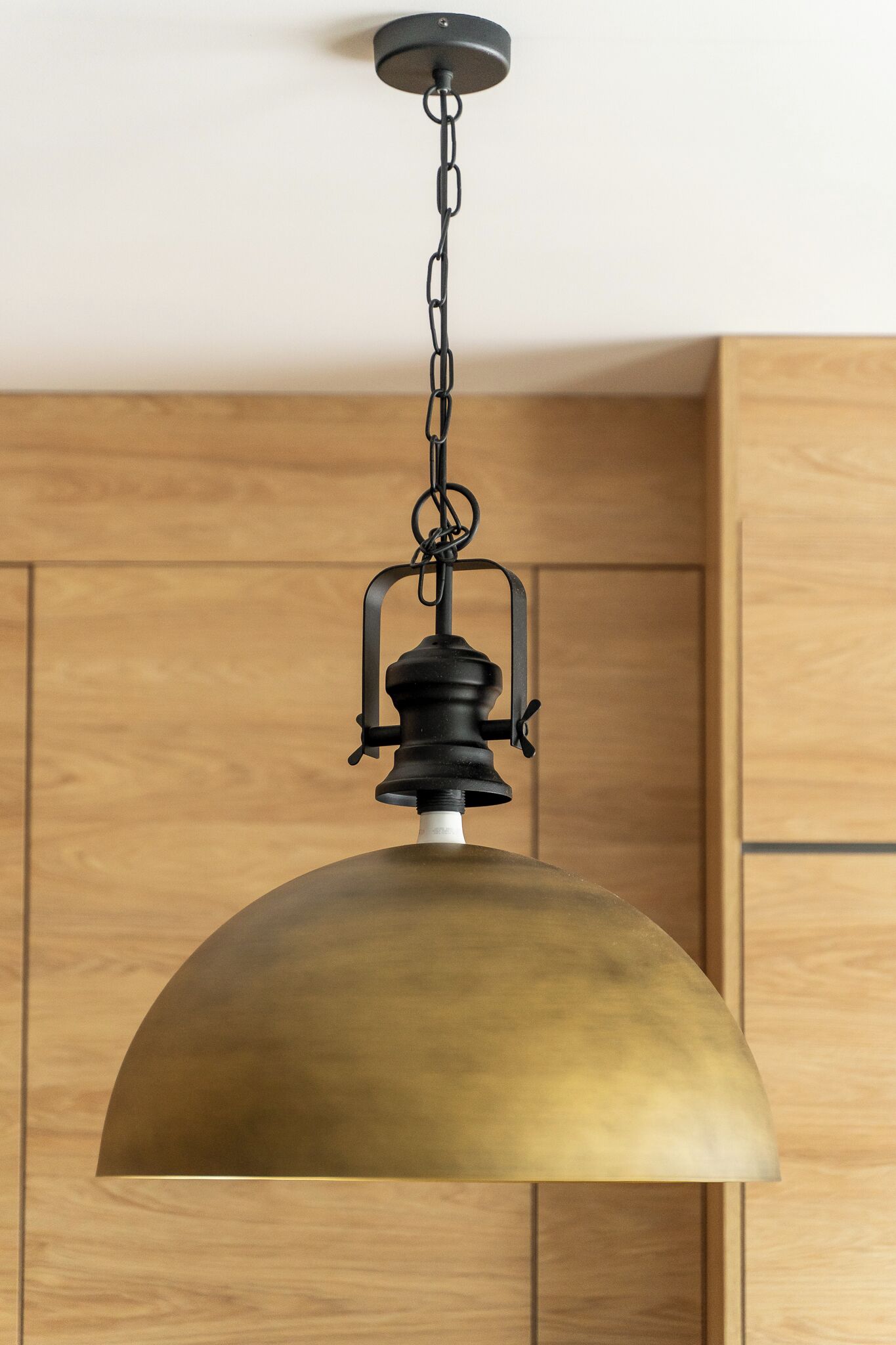 A pendant light with a brass finish hanging from a ceiling chain.