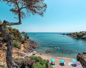 Ein Küstenstrand mit felsigem Gelände, klarem, blauem Wasser und einigen Sonnenschirmen.