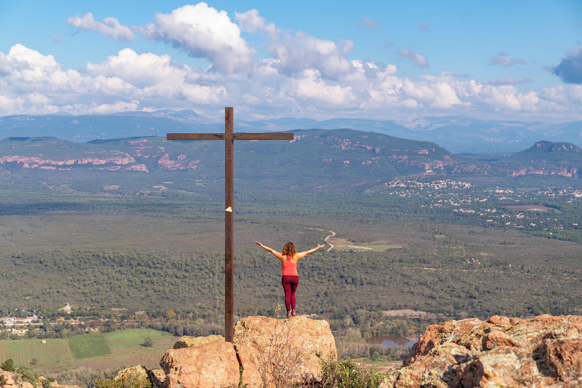Une personne se tient debout sur un rocher, avec une croix en arrière-plan.