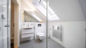 Un baño moderno con piso de diseño geométrico, cabina de ducha de vidrio, lavamanos blanco y un inodoro.