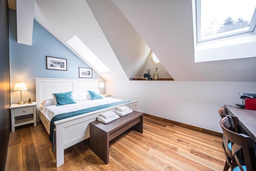 Un dormitorio con cama, mesitas de noche, un banco, un escritorio y una ventana.