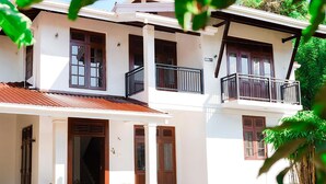 A two-story building with a white facade, wooden doors, and a balcony with a black railing. - Villa Amora Hikkaduwa (Hikkaduwa)