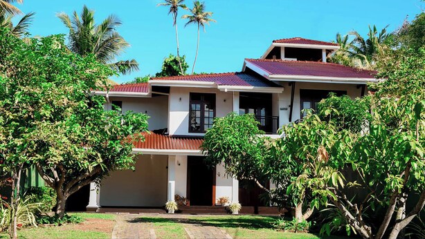 A two-story house with a red roof, surrounded by lush greenery and palm trees. - Villa Amora Hikkaduwa (Hikkaduwa)