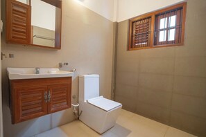 Une salle de bain avec un meuble-lavabo en bois, des toilettes et une fenêtre avec des barreaux.