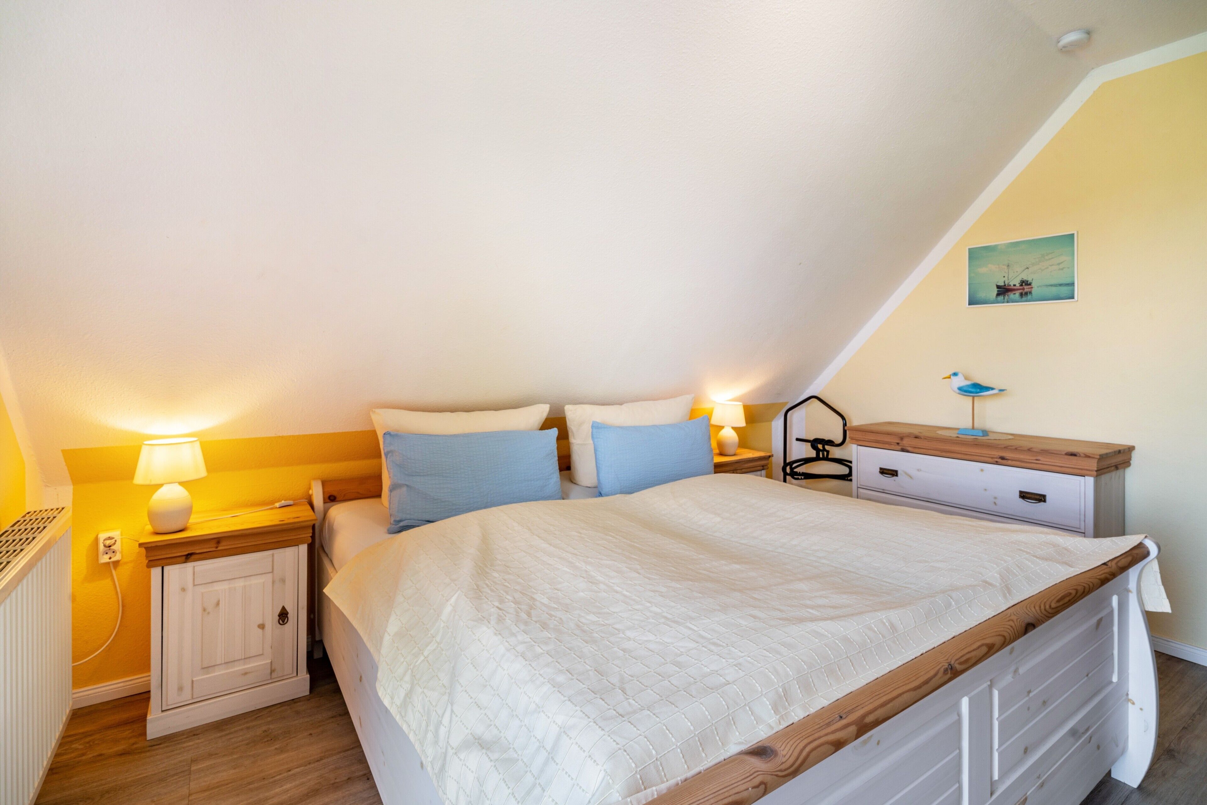 Een slaapkamer met een bed, nachtkastjes, een lamp, een dressoir en een aan de muur hangend schilderij.