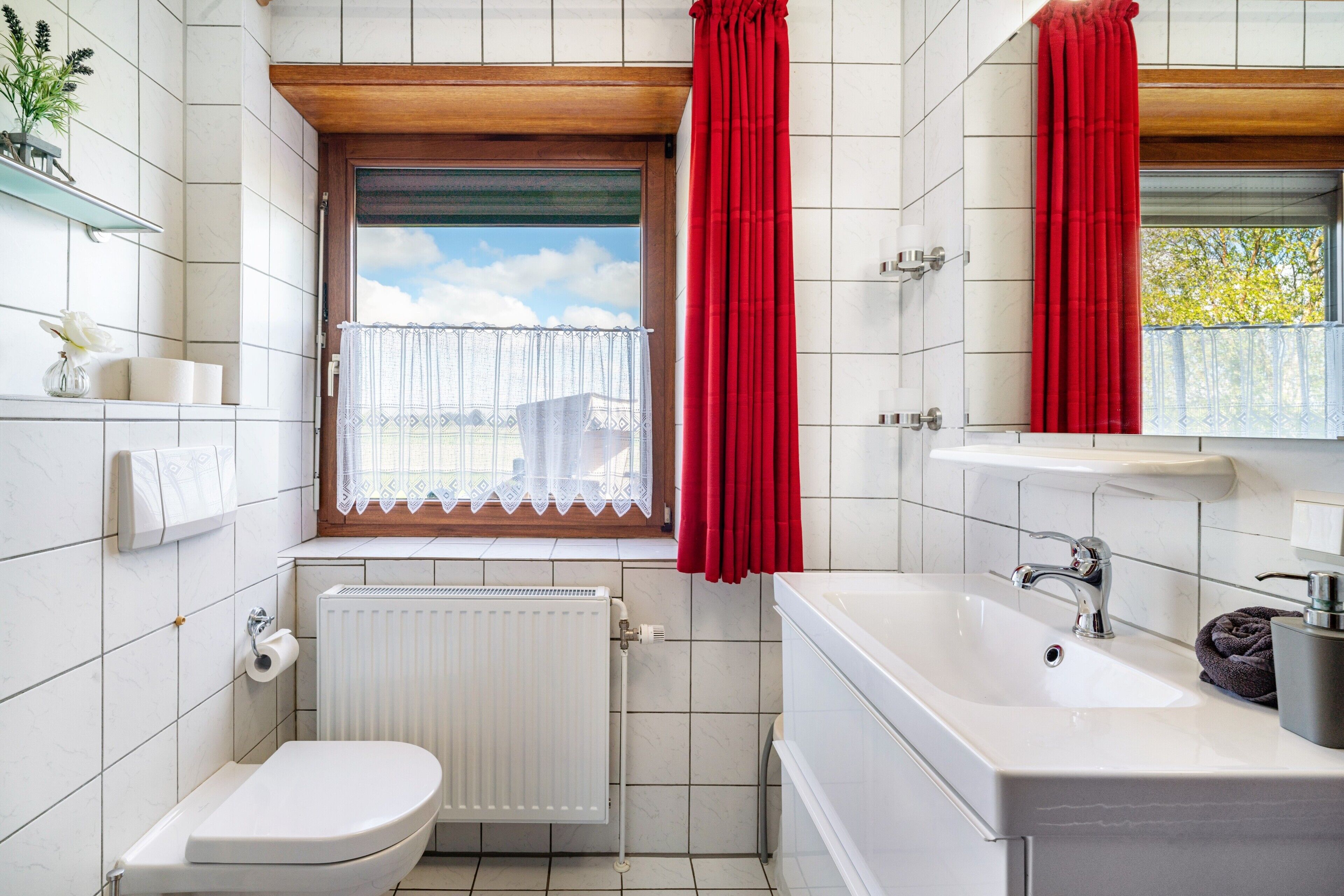 A bathroom with a toilet, a sink, a bathtub, a window with a view, and a radiator.