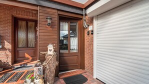 En murbygning med en trædør, en garageport og en lille veranda med dørmåtte og pynt.
