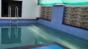 Ein rechteckiger Pool mit einer Leiter, umgeben von einer blauen, strukturierten Wand und einem Abschnitt aus Stein.