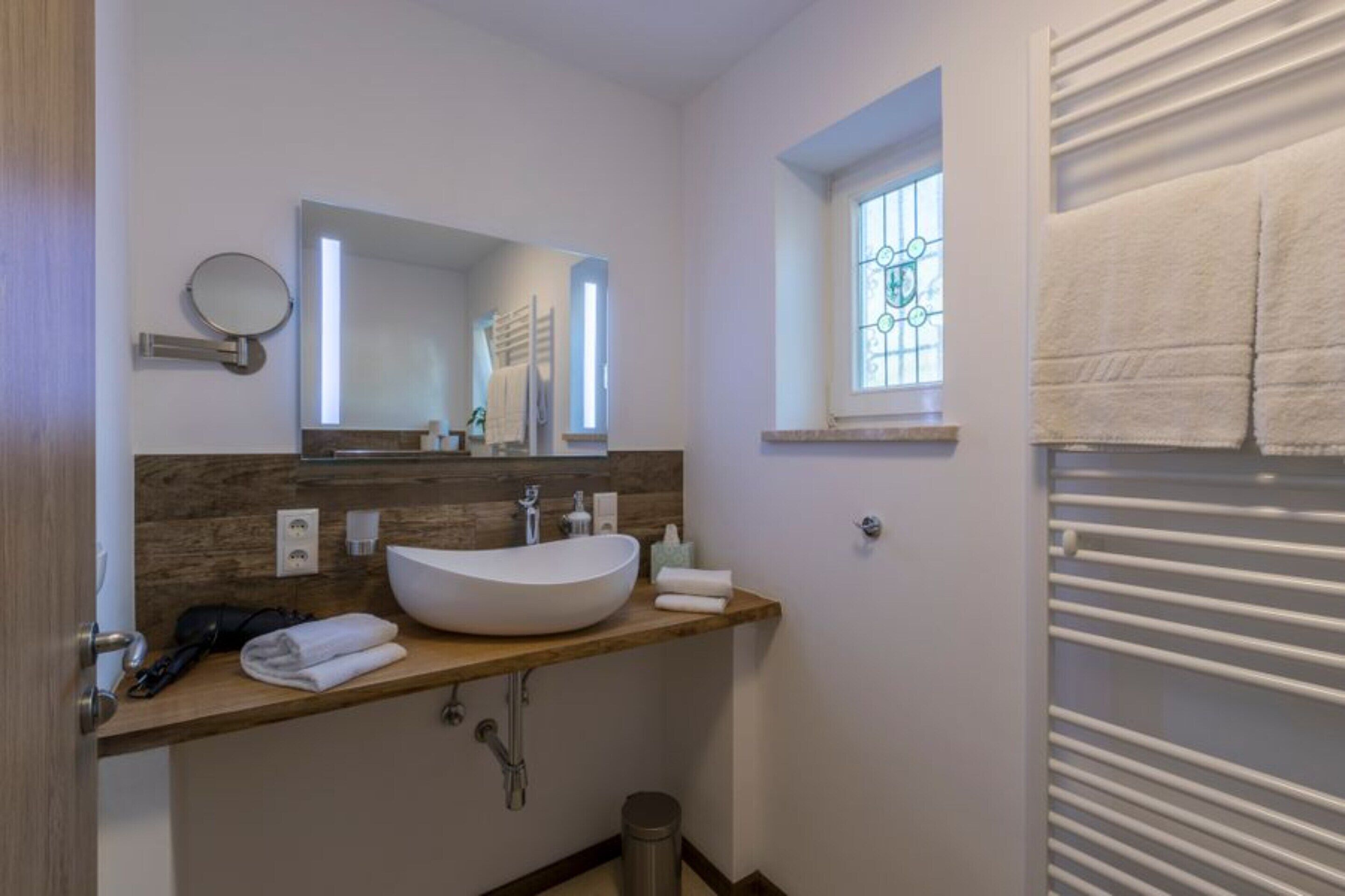 A modern bathroom with a large white sink, a mirror, and a window with a towel rack.