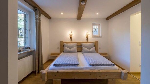 Ein Doppelbett mit Holzrahmen, zwei Nachttische, zwei Wandlampen und ein kleines Fenster mit Blick auf Grünflächen.