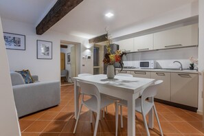Een moderne keuken met witte kastjes, een eettafel met stoelen en een vaas met bloemen.
