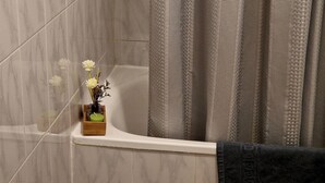 Ein Badezimmer mit einer Badewanne, einem hölzernen Tablett mit Kerze und einer Vase mit Blumen.