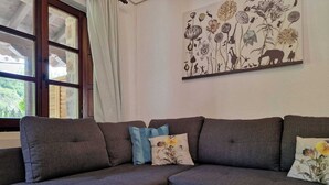 Ein modulares Sofa mit Blumenkissen, ein großes Blumenbild an der Wand und ein Fenster mit Vorhängen.