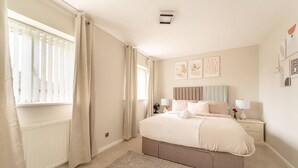 Ein Schlafzimmer mit einem großen Bett, Nachttischen mit Lampen, einem Heizkörper und einem Fenster mit Vorhängen.