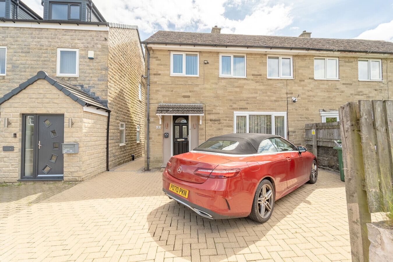 A red car parked in a driveway of a two-story house with a stone facade and a tiled roof.
