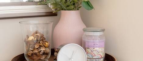A wooden tray on a white dresser with a clock, a jar of wax paper, and a vase with green plants.