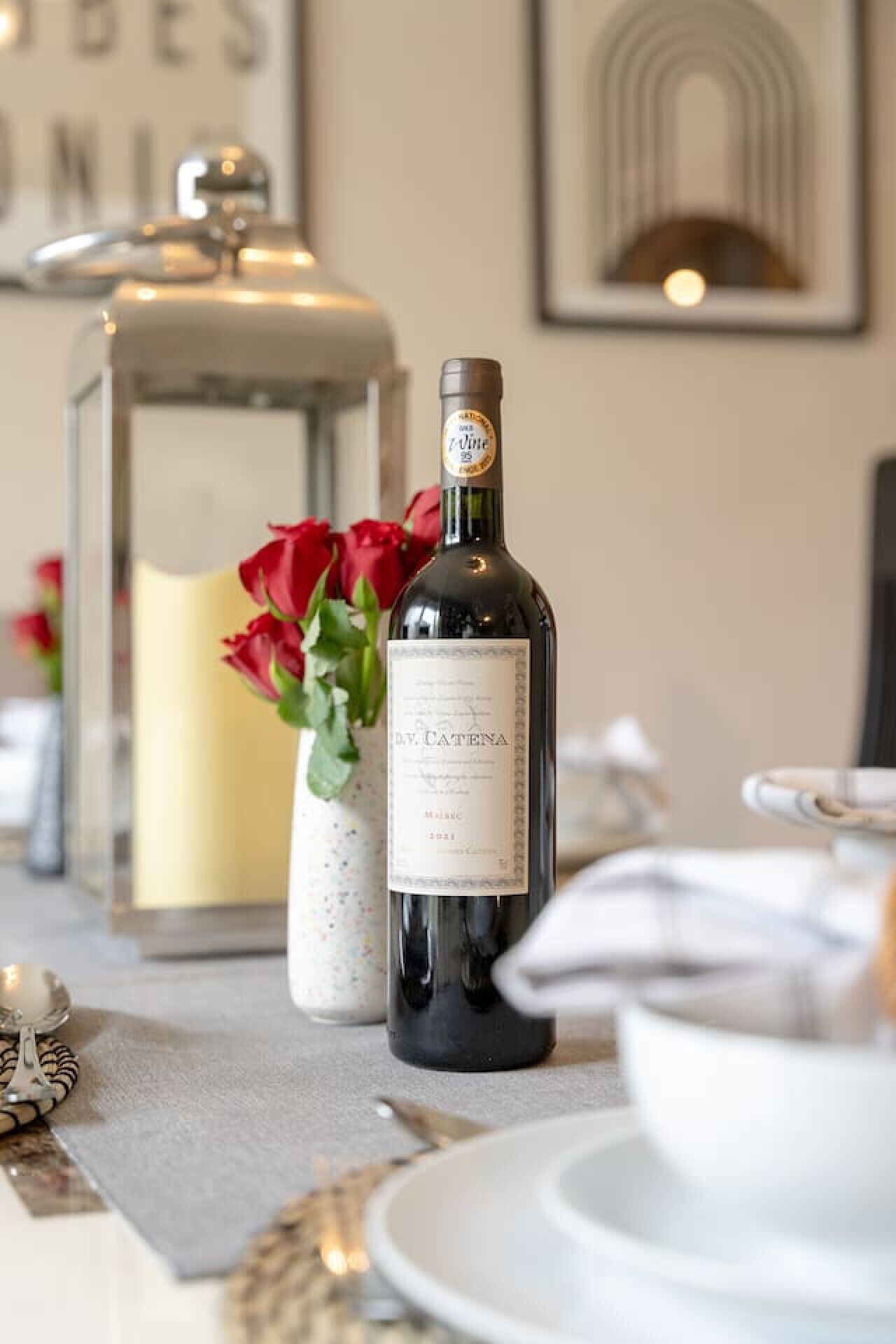 A bottle of wine with a label, a candle, and red roses on a table.