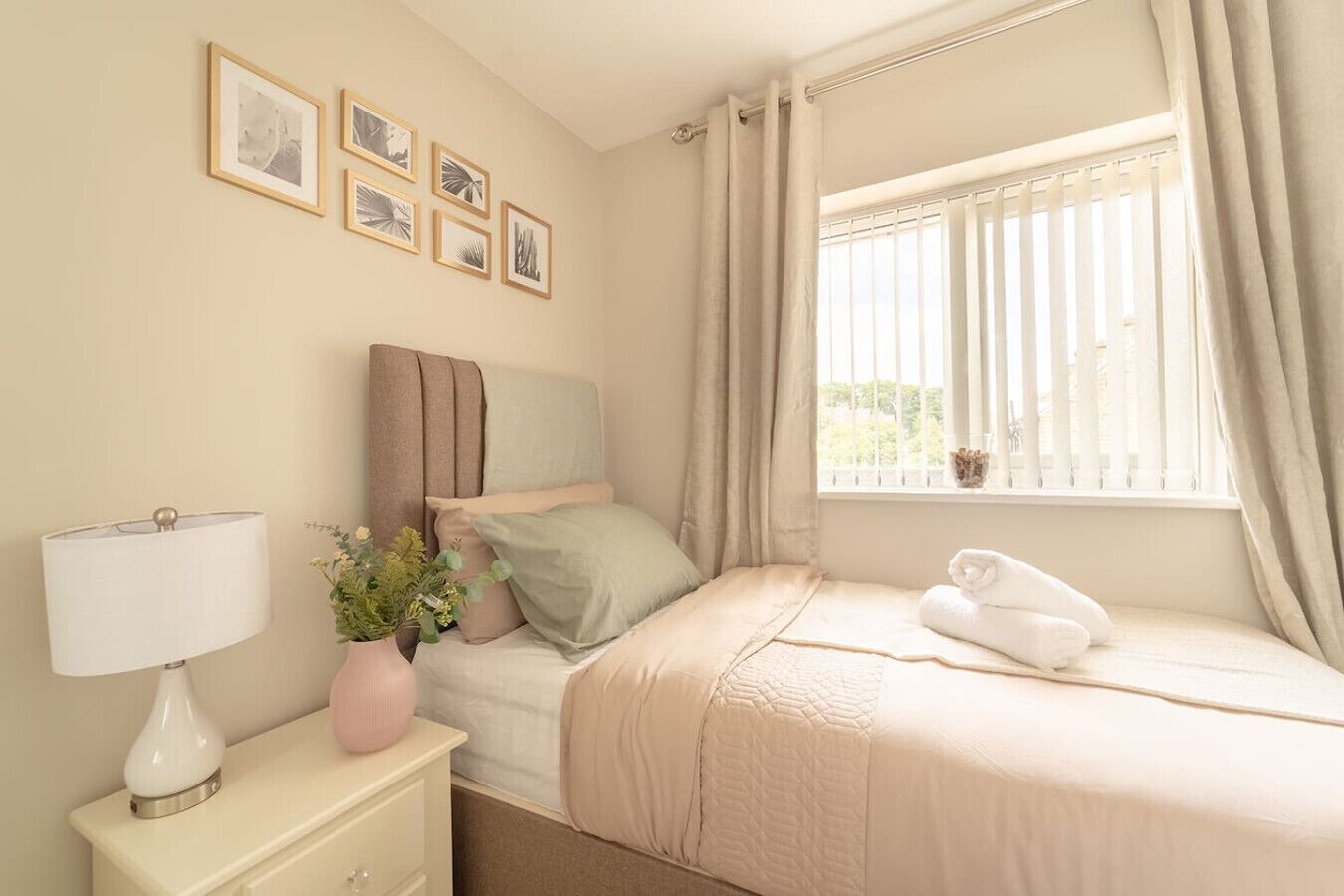 Een keurig opgemaakt slaapkamer met een bed, bedlampje en een raam met gordijnen.