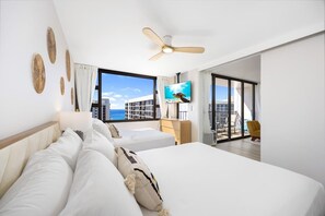 A hotel room with a large bed, a ceiling fan, a TV, and a balcony with a view of the city. - Ocean-view 36th floor lanai w/ free parking (Honolulu)