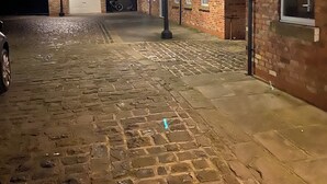 Edifício de tijolos com garagem, entrada por calçada de pedras e um poste de luz.
