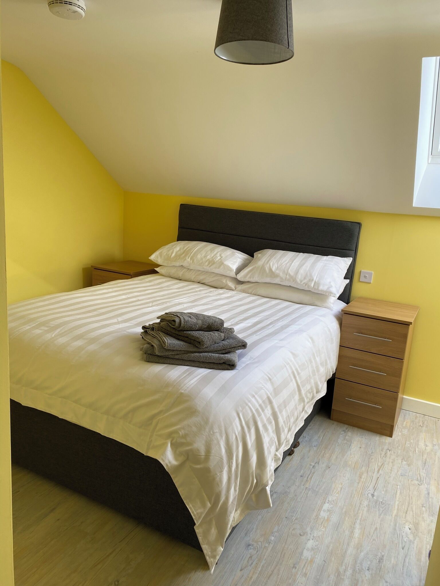 Une chambre à coucher avec un lit, une table de chevet, une lampe et une petite table en bois.