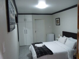Una camera d'albergo con un letto, un armadio, una porta e un piccolo tavolo con una lampada.