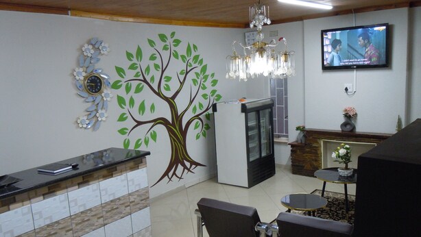 A reception area with a wall mural of a tree, a chandelier, a television, and a reception desk. - Daeka Guesthouse (Kempton Park)