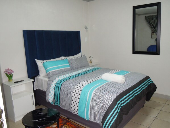 A neatly made bed with patterned bedding, a bedside table with a remote control, and a small vase with flowers.