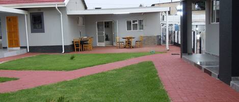 A courtyard with a red brick pathway, a small lawn, and outdoor seating area with tables and chairs.