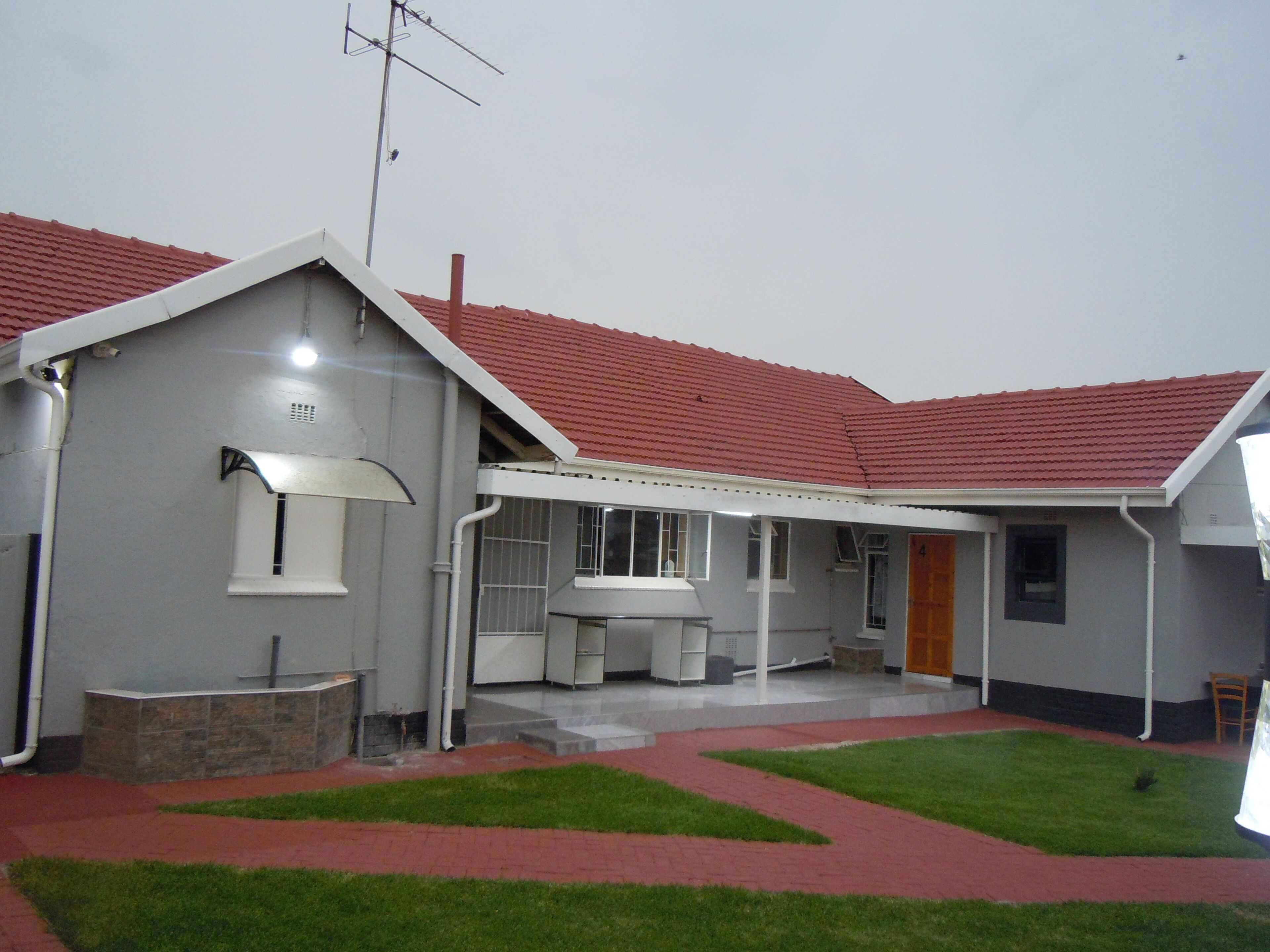 Une maison de plain-pied avec un toit recouvert de tuiles rouges, une terrasse couverte et une petite pelouse.