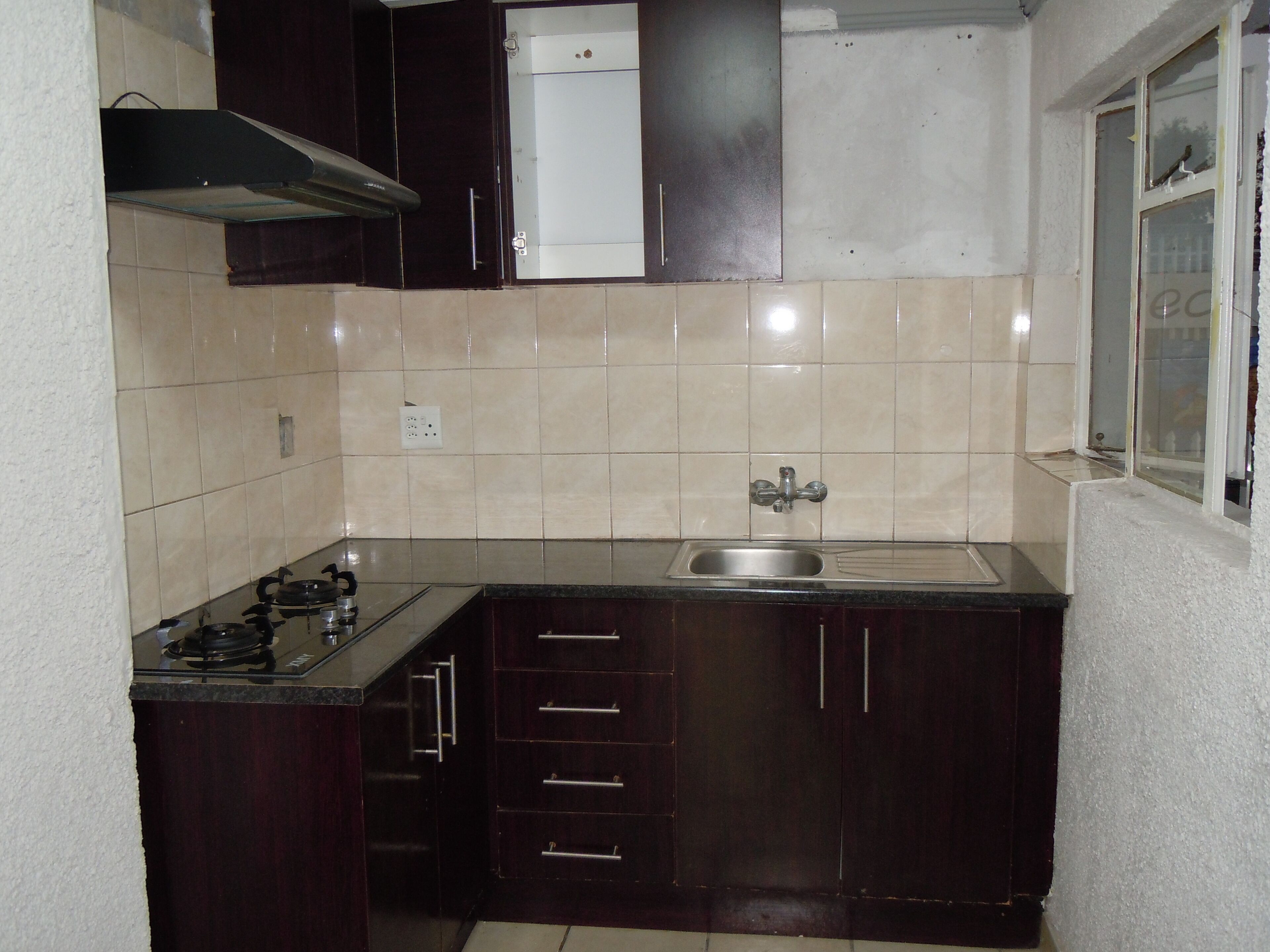 A compact kitchen with dark wood cabinets, a stainless steel sink, and a gas stove.