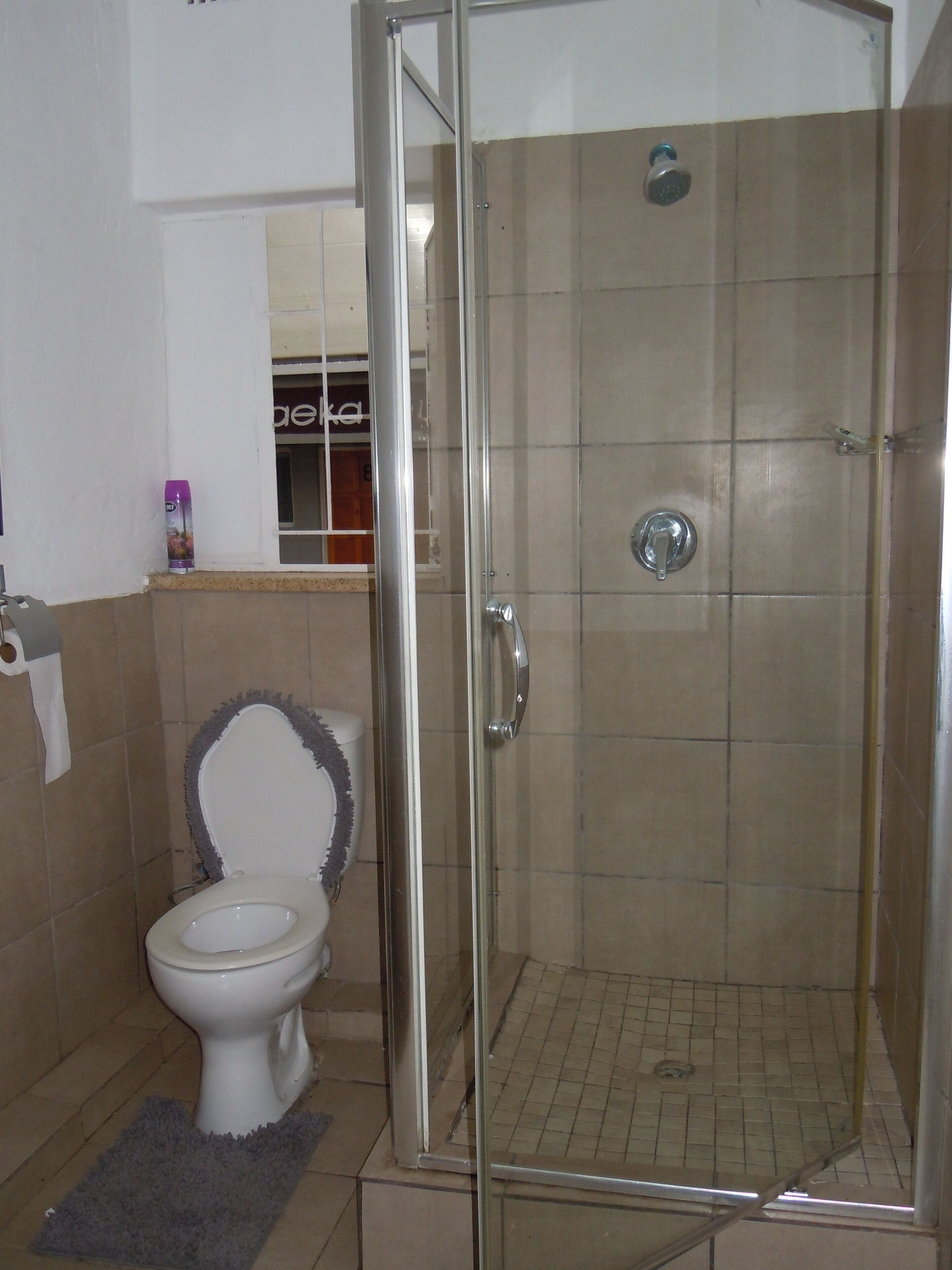 Une salle de bain avec une douche à parois de verre, des toilettes et une petite fenêtre.