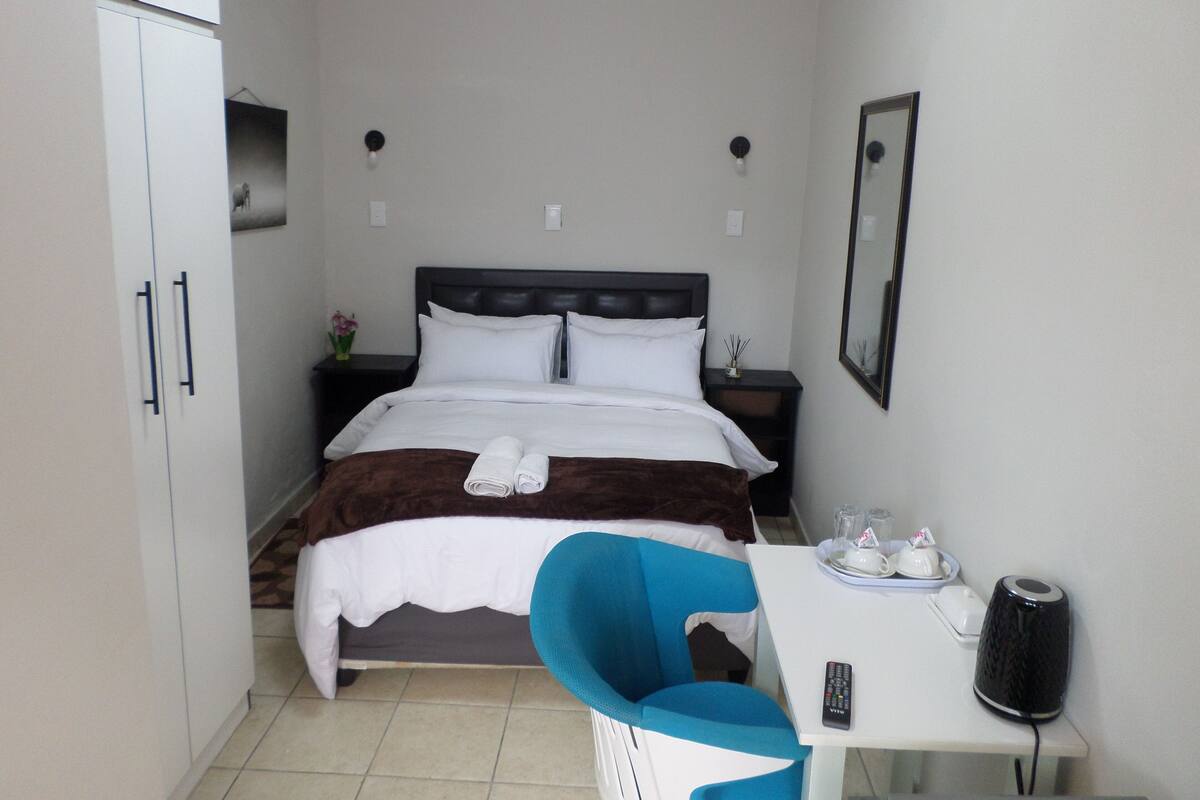 Ein Hotelzimmer mit Bett, Nachttisch, Stuhl und einem kleinen Tisch mit Fernbedienung und Lautsprecher.