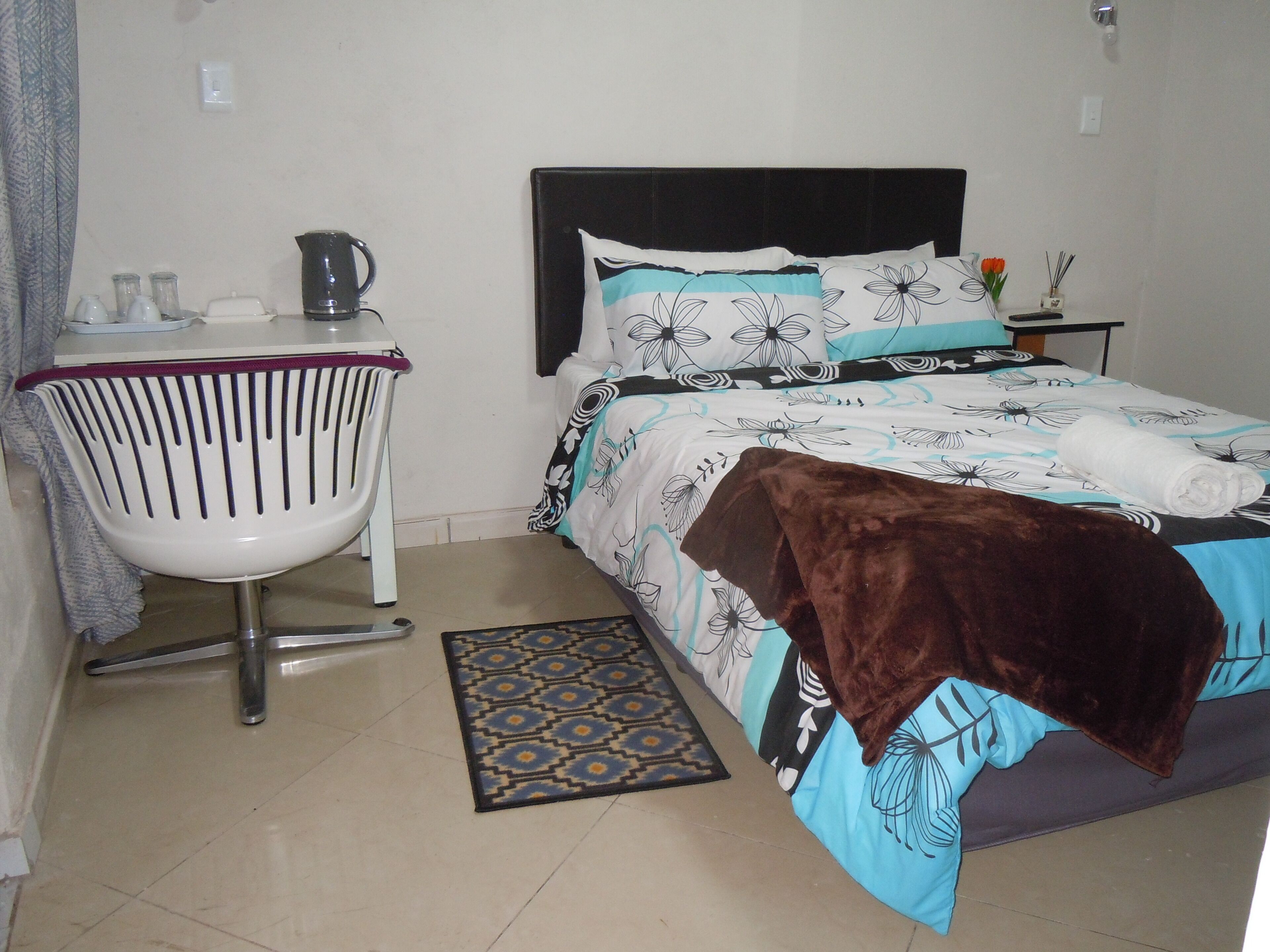 A bedroom with a bed, a chair, a coffee maker, and a small table with a vase.